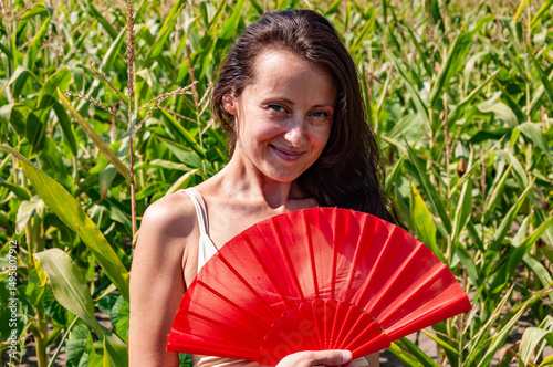Happy woman with smiling face portrait hold red flamenco summer fan in hot cornfield, geisha fashion