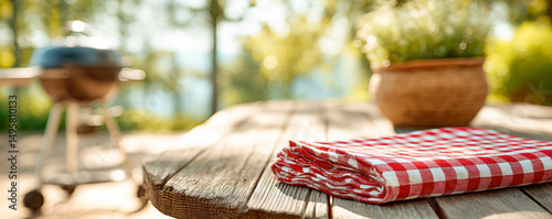 Wooden table with red checkered cloth in backyard garden with grill and BBQ. Back yard party and weekend concept.