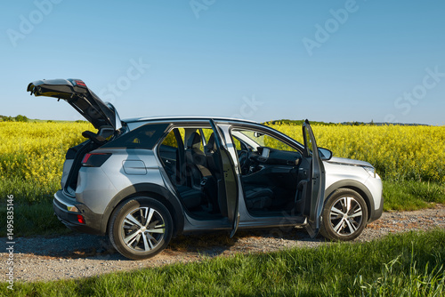 Wallpaper Mural Silver SUV with all doors and trunk open, standing against the background of a field of blooming rapeseed and a cloudless sky. Side view. Torontodigital.ca