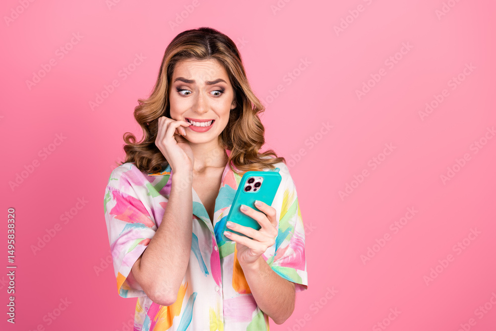 Worried woman wearing a vibrant summer shirt looking perplexed while holding a smartphone on a pink backdrop Worried woman wearing a vibrant summer shirt looking perplexed while holding a smartphone on a pink backdrop