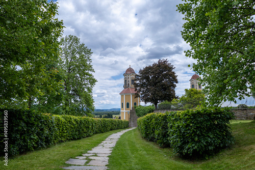 European Heritage Church with Scenic Walkway. A charming historic church stands at the end of a stone path, surrounded by flourishing trees and open skies.