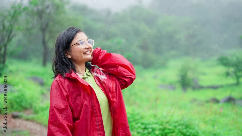 Portrait of beautiful Indian girl enjoying rain while standing in forest. Carefree female tourist in rain. Rain drops falling on face. Positive girl smiling and enjoying the rain outdoors.