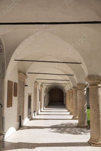 Historic Arched Corridor with Stone Columns. A serene, sunlit arched corridor with stone columns and plaques on the walls.