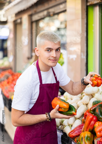 Wallpaper Mural Young guy seller in apron puts fresh bell pepper on display at vegetable market Torontodigital.ca