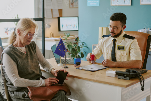 Slika na platnu Senior woman sitting at immigration office with officer checking her documents