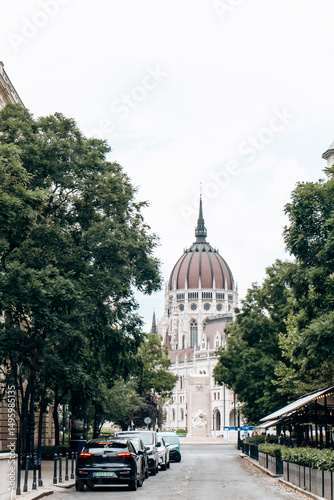 Wallpaper Mural Budapest, July 25: A breathtaking scenic street view showcasing an iconic building surrounded by trees and parked cars Torontodigital.ca