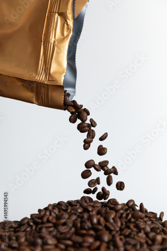 Coffee beans falling out of a packaging against a white background. The packaging is positioned at the top, with coffee beans suspended in mid-air and a pile of beans visible at the bottom.