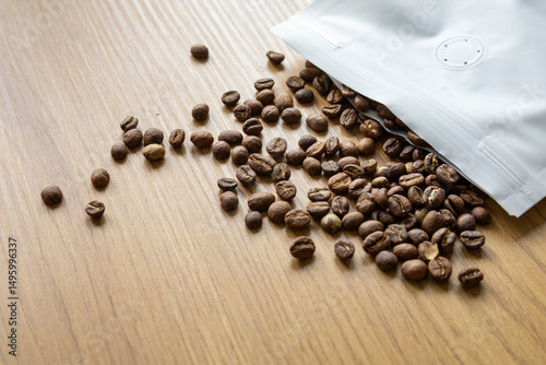 Medium roasted coffee beans spilled out of a white paper bag onto a wooden surface.