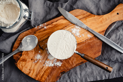Leveled Measuring Cup of All-Purpose Flour: Directly above one leveled cup of flour with spoon, knife, cutting board, and jar of flour
