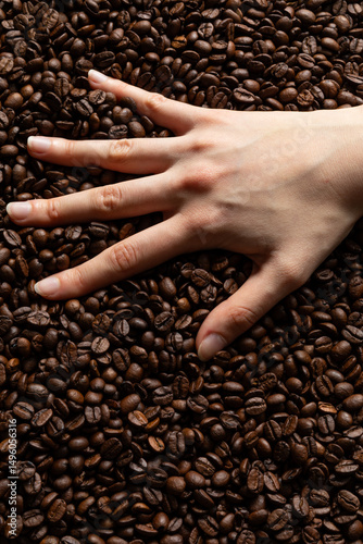 A close-up view of a hand placed on a layer of roasted coffee beans
