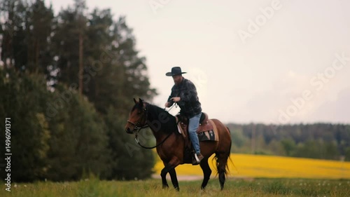 cowboy man in hat riding horse across meadow