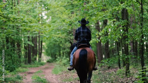 cowboy in a hat rides a horse through the forest