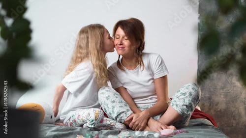 Little girl looks lovingly at mother as they sit together in cozy bedroom. Moments of warmth, care and silent communication between mother and daughter enjoying time and beauty activities.