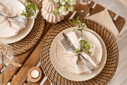 Elegant table setting with plates, burning candle and blooming tree branches, closeup