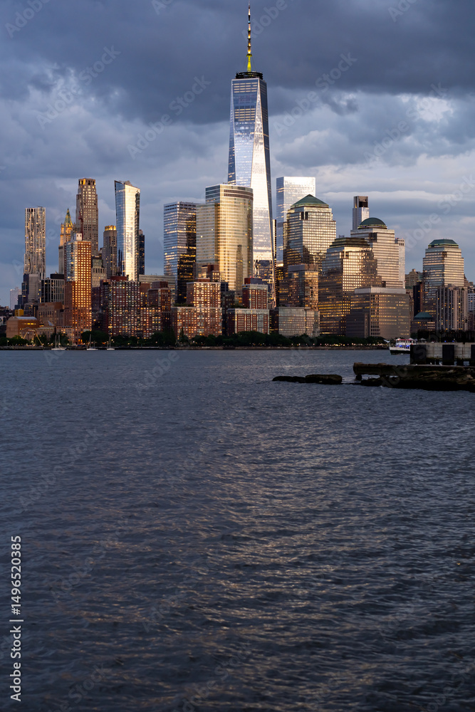 Fototapeta premium New York city. NYC cityscape. Lower Manhattan and One World Trade Center in New York Cit. Skyscrapers of Manhattan located near rippling water of New York bay against blue sky. New York skyscrapers.