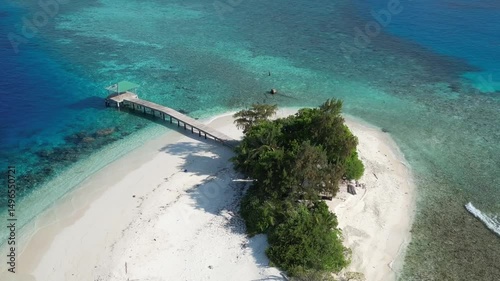 Aerial view of desert island in blue sea. Lonely building and pier at the coastline. Maldives