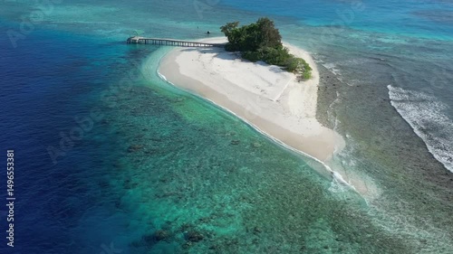 Aerial view of small lonely island in Indian Ocean at sunny day. Beautiful coral reef in transparent tropical water.Private jetty and small house at the beachfront