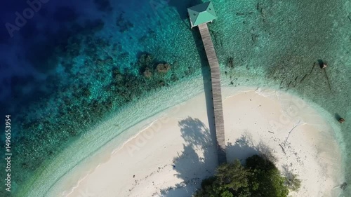 Aerial view of small lonely island in Indian Ocean at sunny day. Beautiful coral reef in transparent tropical water.Private jetty and small house at the beachfront