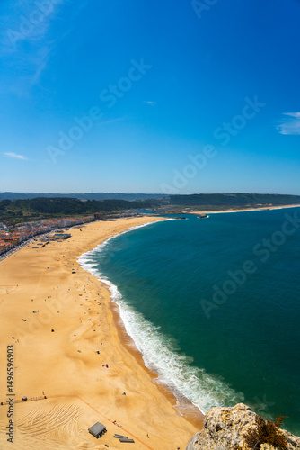 Aerial perspective of the sweeping golden coastline of Nazaré beach under clear sky
