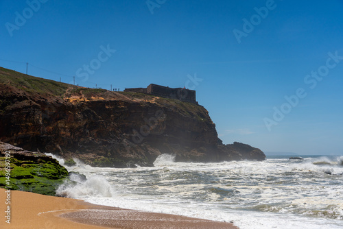 Farol da Nazaré stands atop the cliff as powerful waves crash below