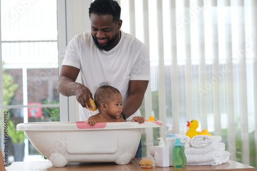 African family, father bathing kid in tub, dad washing and cleaning his little toddler girl daughter child in bath. Cheerful toddle baby infant having fun while taking bubble bath in bathroom.

