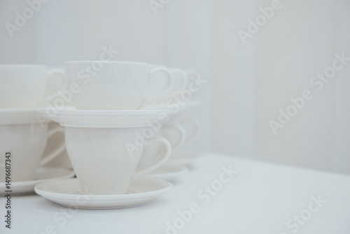 Lots of empty tea or coffee cups on a white table against a white wall, space for text.  Organization of events, catering, catering, beautiful white and gray background