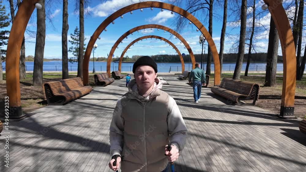 Young man nordic walking in a spring beautiful park by the lake. outdoor trekking, active walking.