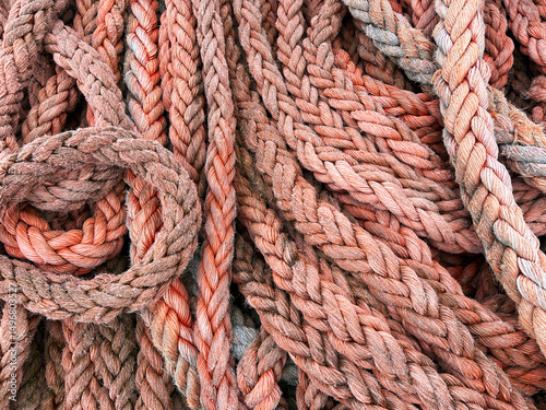 Thick weathered marine ropes coiled and tangled in a pile, showcasing textures and natural wear in a muted red hue