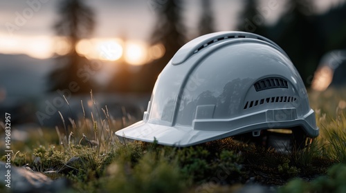 White construction safety helmet placed on grassy field at sunrise with blurred forest background — concept of work-life balance, environmental building, and labor pause moments photo