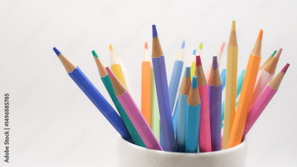Fototapeta premium A collection of multicolored pencils arranged in a white ceramic cup against a bright, clean background
