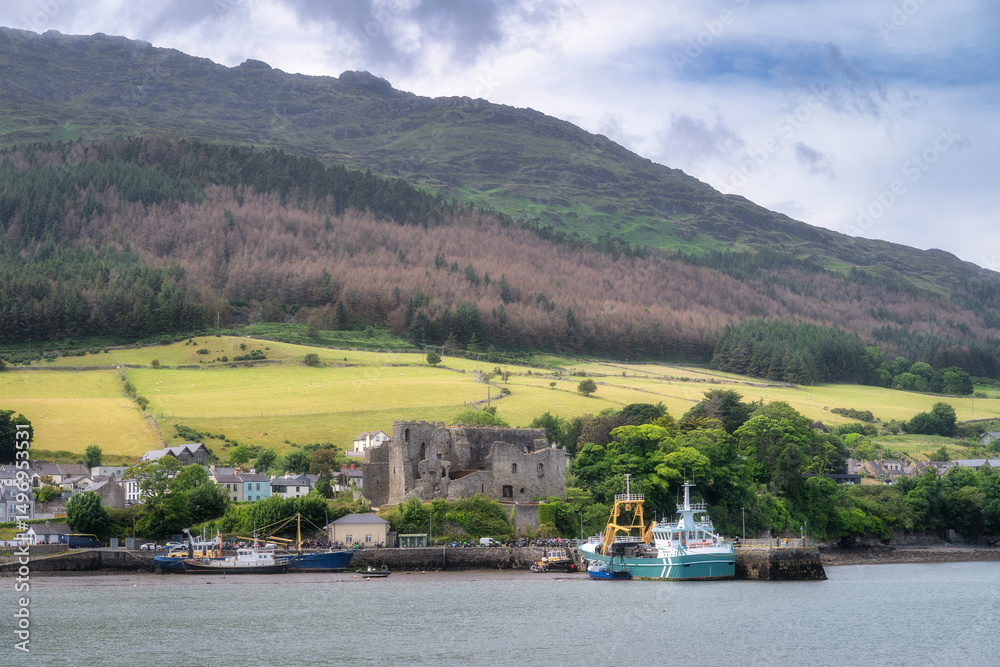 Obraz premium A picturesque harbor that boasts charming fishing boats, surrounded by lush green hills and historical remnants, all set beneath a beautifully clouded sky, Carlingford, Ireland