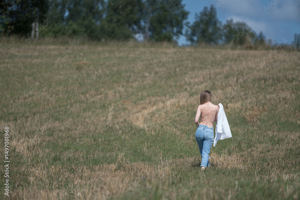 Caucasian 20s Woman Strolling Through Open Field Holding White Shirt and Facing Away Caucasian 20s Woman Strolling Through Open Field Holding White Shirt and Facing Away
