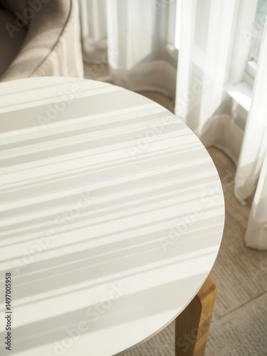 Modern round tabletop bathed in striped sunlight from a nearby window