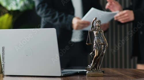 On the table is a laptop and a statue of justice. Unrecognizable business people are discussing task allocation. The concept of legal support and counseling.