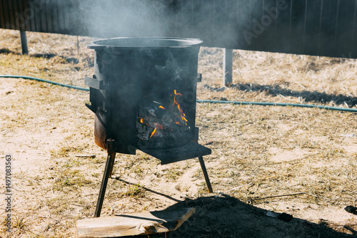 Steel kazan, a large cast iron cauldron, on a fire pit for cooking outdoors. Outdoor cooking concept with wood burning stove.