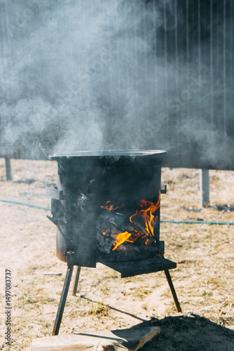 Steel kazan, a large cast iron cauldron, on a fire pit for cooking outdoors. Outdoor cooking concept with wood burning stove.