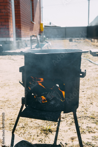 Outdoor cooking fire in a metal stove. Flame and smoke coming from burning wood in a campfire oven for camp meal preparation.