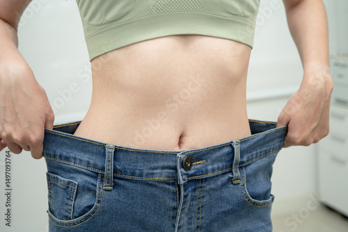Young Asian woman losing weight wearing loose pants in oversize jeans.
