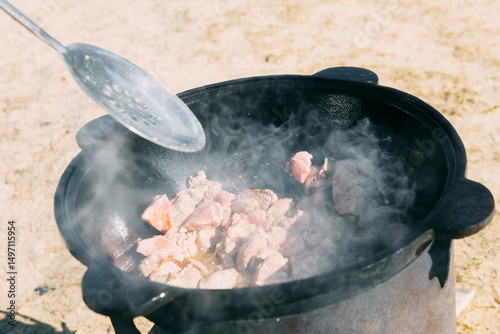 Meat cooking in a large cauldron outdoors over an open fire, a classic outdoor cooking concept for camping and traditional cuisine.
