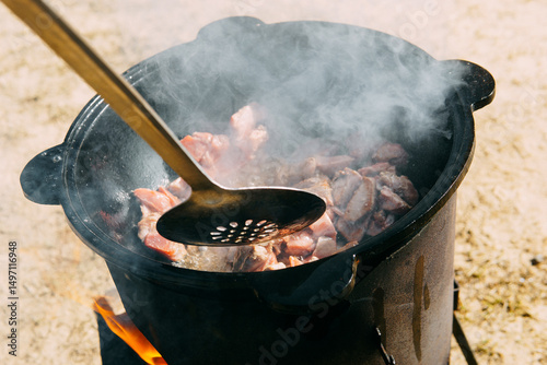 Meat cooking in a large cauldron outdoors over an open fire, a classic outdoor cooking concept for camping and traditional cuisine.