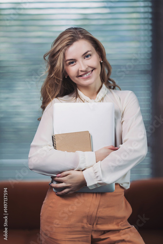 Smiling young woman holds notebooks in modern office environment during morning work hours
