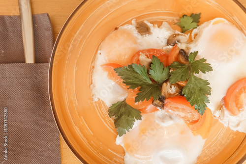 Close up view of fried eggs with tomatoes, mushrooms and parsley on a plate. Breakfast dish on a wooden table. Healthy and fresh morning meal for dining.