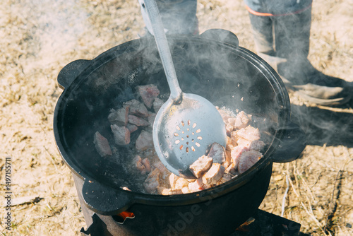 Meat cooking in a large cauldron outdoors over an open fire, a classic outdoor cooking concept for camping and traditional cuisine.