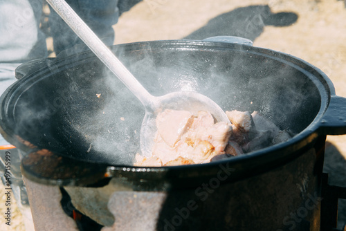 Meat cooking in a large cauldron outdoors over an open fire, a classic outdoor cooking concept for camping and traditional cuisine.
