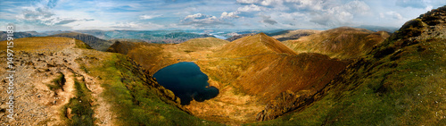 Mountain lake in panoramic view. Aerial landscape of rugged peaks, hiking trails, blue tarn. Helvellyn, English Lake District. Remote wilderness terrain for trekking, eco-tourism, outdoor adventure