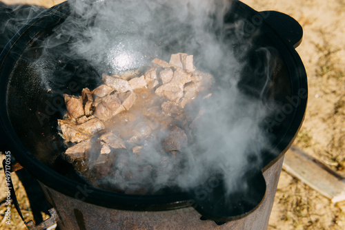 Pieces of meat frying in oil in a large cast iron cauldron with steam. Cooking outdoor in a big pot for holiday.