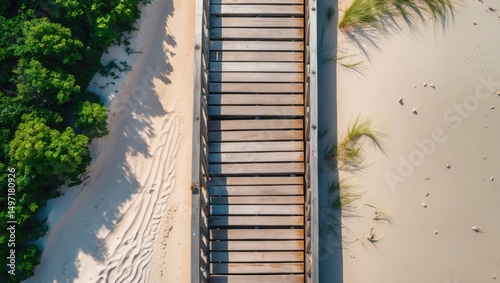 Aerial view of a wooden boardwalk on a sandy beach with greenery and shadows.