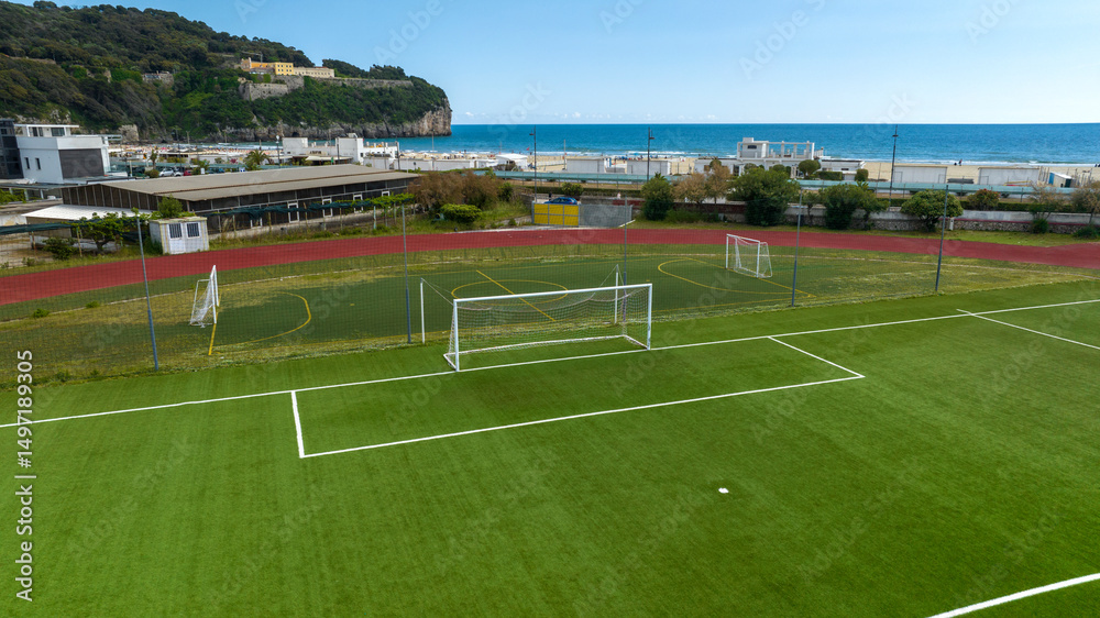 Fototapeta premium Aerial view of a goal in a soccer field. The synthetic grass soccer field is empty and there are no players. In the background there is sea and a beach.
