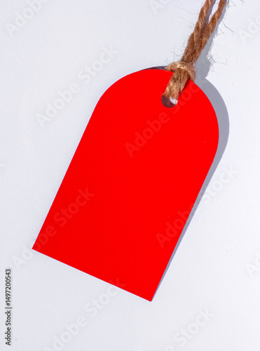 Red Price Tag. Red Empty Cardboard Tag on a White Background. Red Paper Tag With Copy Space.  Discount Label Hanging On a Cord, Ideal For Sale, Promotion. 