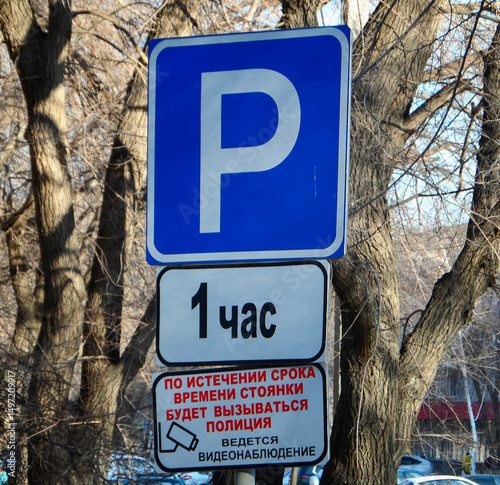Parking sign in a city with 1-hour limit, police warning, and video surveillance notice. Urban scene with bare trees in background. Ust-Kamenogorsk (kazakhstan) photo